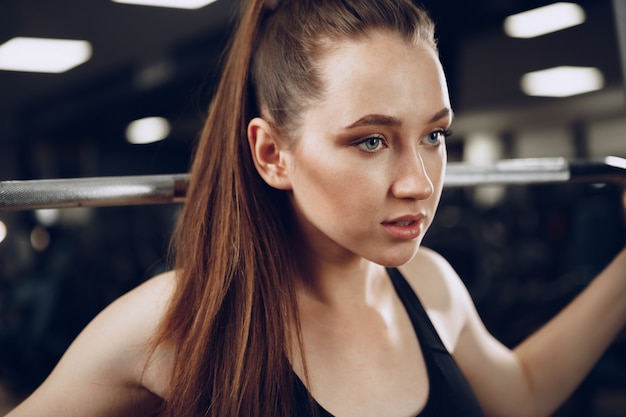 Mujer joven atractiva haciendo ejercicios para los músculos de los brazos y la espalda en un gimnasio