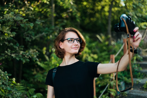 Foto mujer joven atractiva hipster chica toma retrato selfie con cámara retro al aire libre