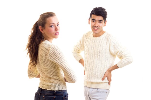 Una mujer joven y atractiva con un hombre joven y atractivo con suéteres blancos y jeans de pie en el estudio