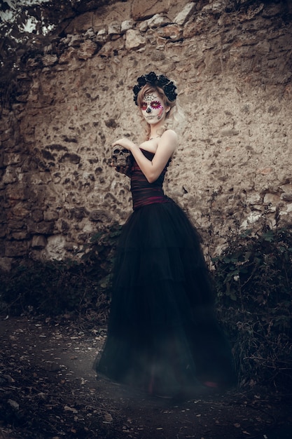 Mujer joven atractiva con maquillaje de calavera de azúcar. Día mexicano de la mujer muerta con maquillaje de calavera de azúcar y corona de flores.