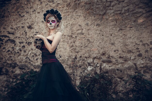 Mujer joven atractiva con maquillaje de calavera de azúcar. Día mexicano de la mujer muerta con maquillaje de calavera de azúcar y corona de flores.