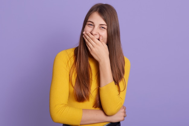 La mujer joven atractiva parece feliz y emocionada, sorprendida y asombrada cubriendo la boca con las manos, expresión linda mujer, posando contra la pared de color lila.