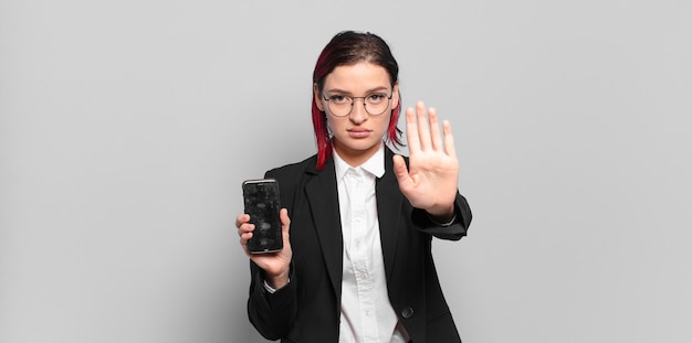 Mujer joven atractiva pelirroja que parece seria, severa, disgustada y enojada mostrando la palma abierta haciendo gesto de parada. concepto de negocio