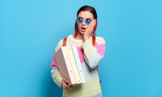 Mujer joven atractiva pelirroja que se siente feliz, emocionada y sorprendida, mirando hacia el lado con ambas manos en la cara. concepto de estudiante universitario