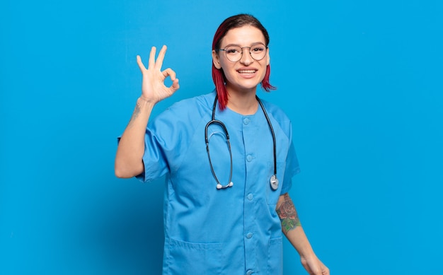 Mujer joven atractiva pelirroja que se siente feliz, relajada y satisfecha, mostrando aprobación con gesto bien, sonriendo. concepto de enfermera del hospital