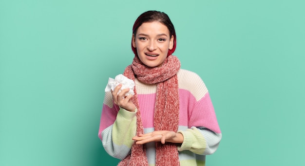 Mujer joven atractiva pelirroja sonriendo alegremente, sintiéndose feliz y mostrando un concepto en el espacio de la copia con la palma de la mano concepto de gripe