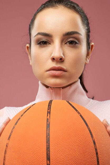 Mujer joven atractiva con pelota de baloncesto posando en el estudio