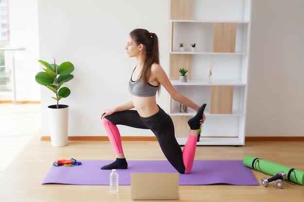 Mujer joven atractiva que hace yoga que estira yoga en línea en casa.