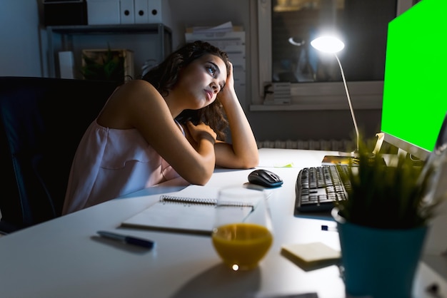 Mujer joven atractiva que trabaja en oficina del coworking en la noche. Chica usando escritorio contemporáneo