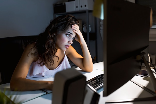 Mujer joven atractiva que trabaja en oficina del coworking en la noche. Chica usando escritorio contemporáneo