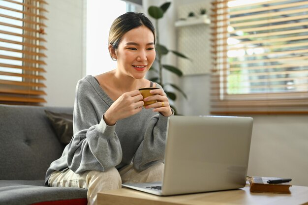 Mujer joven atractiva que usa una computadora portátil en casa navegando por Internet viendo películas y comprando en línea