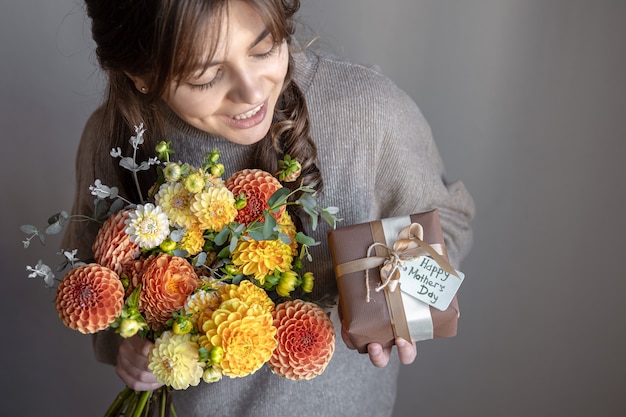 Mujer joven atractiva con un regalo del día de la madre y un ramo de flores de crisantemo en sus manos.