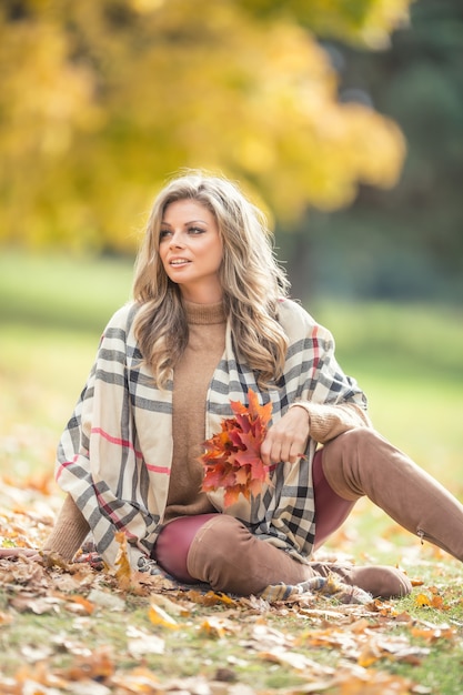 Mujer joven atractiva con sonrisa sensual sentada en el parque de otoño.