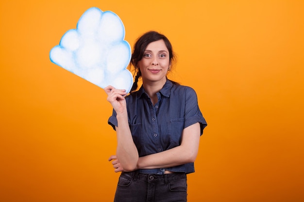 Mujer joven atractiva sosteniendo una nube de ideas en el estudio sobre fondo amarillo. Mujer joven alegre con actitud positiva. Copie el espacio disponible.