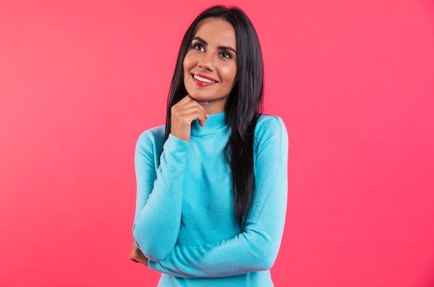 Mujer joven atractiva en un suéter de cuello alto azul está posando delante y sonriendo y mirando hacia adelante