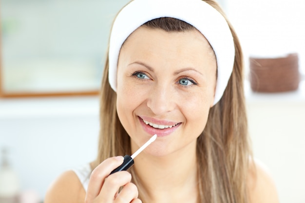 Mujer joven atractiva usando lipgloss en el baño