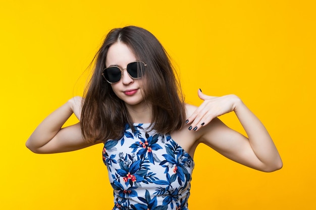 Mujer joven atractiva con un vestido y gafas de sol sobre un fondo amarillo