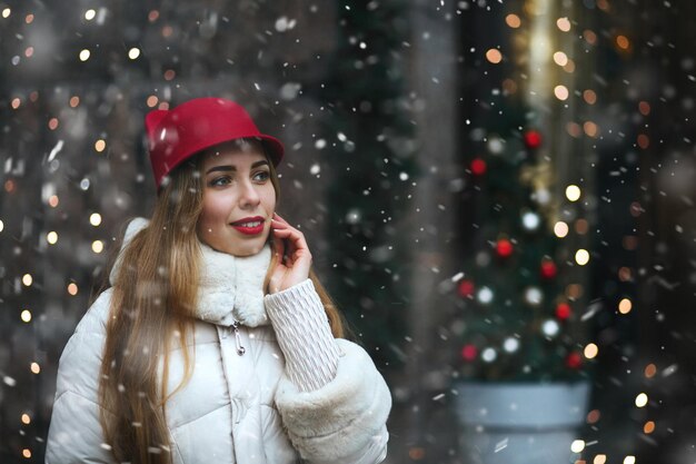 Mujer joven atractiva viste gorra roja caminando por la calle decorada con guirnaldas. Espacio vacio