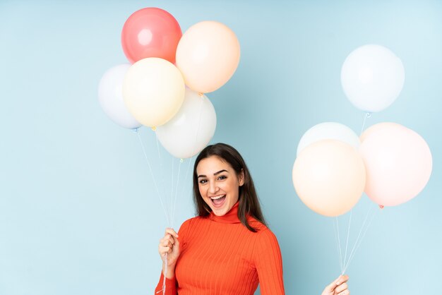 Mujer joven atrapando muchos globos aislados en la pared azul