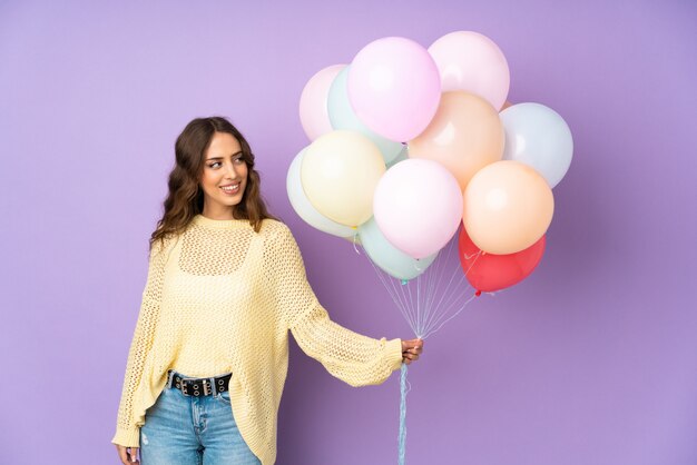 Mujer joven atrapando muchos globos al mirar hacia el lado