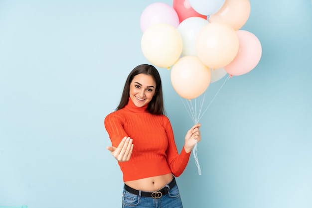 Mujer joven atrapando muchos globos en azul invitando a venir