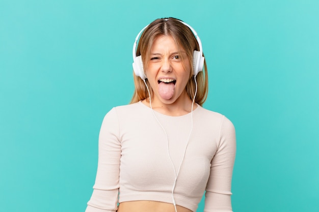 Mujer joven con auriculares con actitud alegre y rebelde, bromeando y sacando la lengua