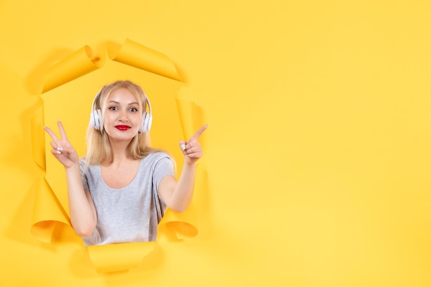 Mujer joven en auriculares apuntando a algo sobre ultrasonido de sonido de audio de fondo amarillo