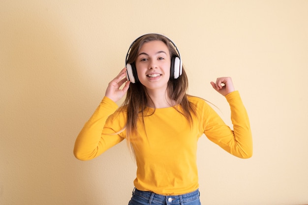 Mujer joven con auriculares bailando sobre fondo amarillo