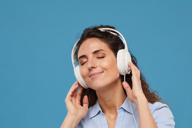 Mujer joven en auriculares escuchando música contra el fondo azul.