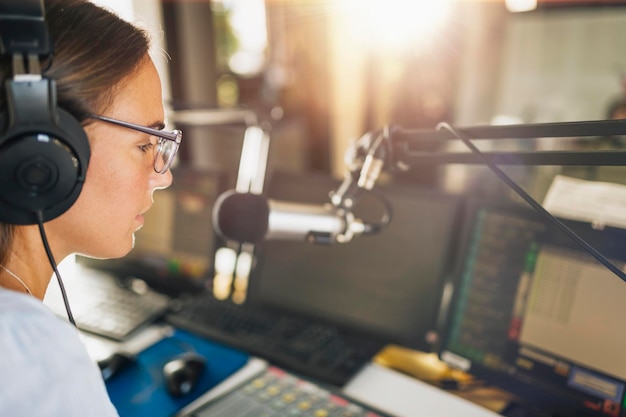 Foto mujer joven con auriculares hablando con la audiencia desde su estudio de podcast