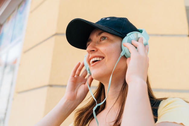 Mujer joven con auriculares de menta y gorra negra afuera en la calle