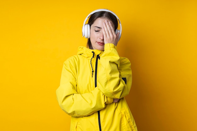 Mujer joven en auriculares con los ojos cerrados en una chaqueta amarilla sobre un fondo amarillo