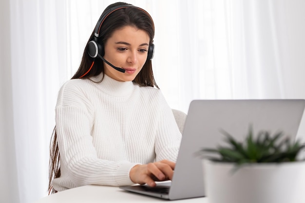 Mujer joven con auriculares que trabaja en línea a través de una computadora portátil