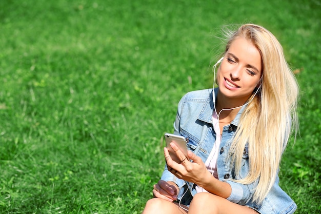 Mujer joven con auriculares y smartphone escuchando música sobre el césped