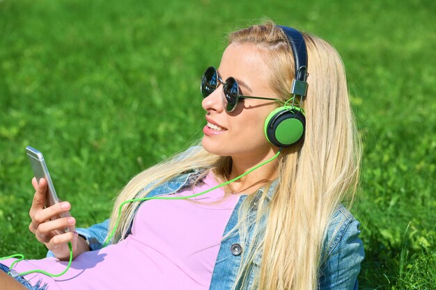 Mujer joven con auriculares y smartphone escuchando música sobre el césped