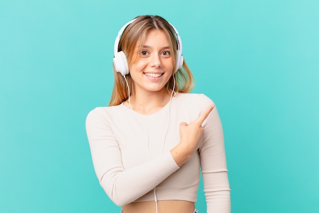 Mujer joven con auriculares sonriendo alegremente, sintiéndose feliz y apuntando hacia un lado