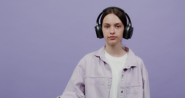 Una mujer joven con auriculares sostiene un móvil en la mano con la pantalla hacia adelante