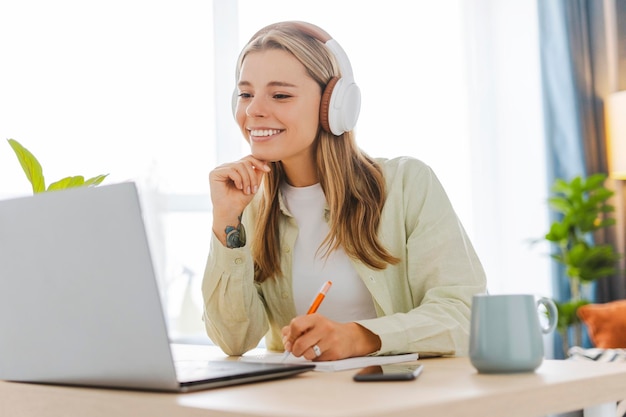 Mujer joven con auriculares tomando notas mientras asiste a una clase en línea