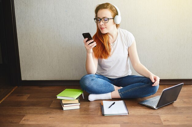 Mujer joven con auriculares trabaja o estudia en un portátil sentado en el suelo de la casa. Concepto de oficina en casa. Trabajar desde casa