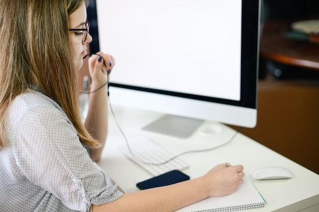 Mujer joven con auriculares trabajando, aprendiendo, hablando por computadora.