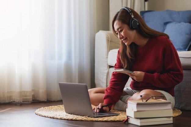 Una mujer joven con auriculares usando una computadora portátil para el estudio en línea en casa
