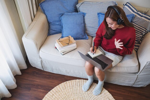 Una mujer joven con auriculares usando una computadora portátil para el estudio en línea en casa