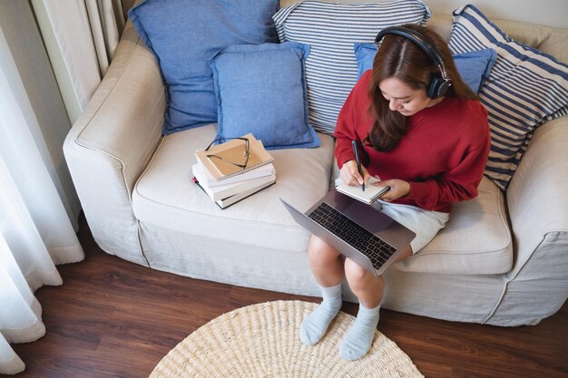 Una mujer joven con auriculares usando una computadora portátil para el estudio en línea en casa
