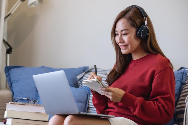 Una mujer joven con auriculares usando una computadora portátil para el estudio en línea en casa