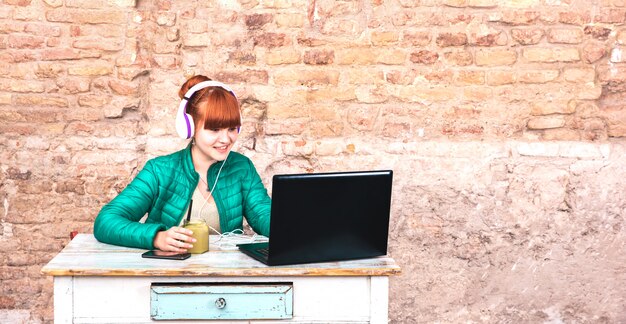 Mujer joven con auriculares usando laptop en la oficina de la casa