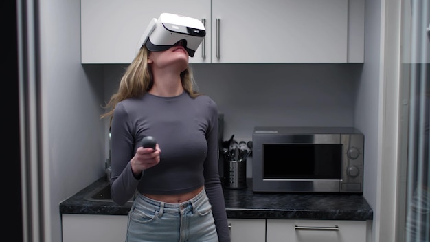 Mujer joven con auriculares vr y joystick de pie en una cocina pequeña