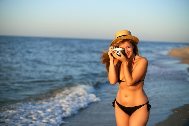 Mujer joven auténtica con cámara de película retro vintage disfrutando de la playa tropical en vacaciones de verano