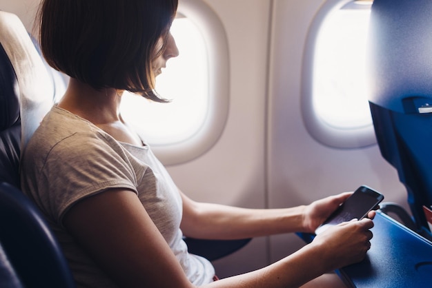 Mujer joven en un avión con un teléfono inteligente en las manos