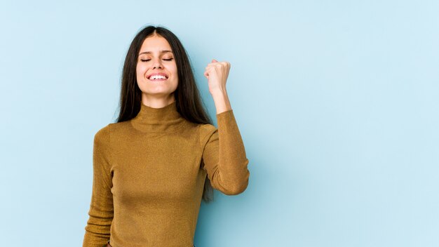 Mujer joven en azul celebrando una victoria, pasión y entusiasmo, feliz expresión.