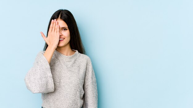 Mujer joven en azul divirtiéndose cubriendo la mitad de la cara con la palma.